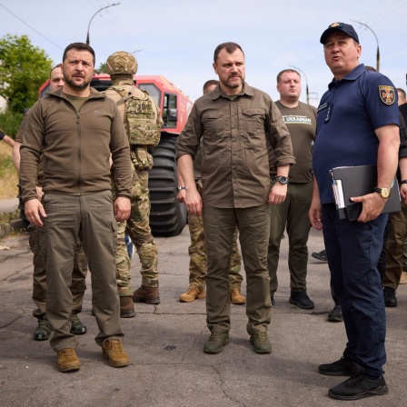 Der ukrainische Präsident Selenskyj und mehrere weitere Männer in Uniform stehen auf einer Straße in Cherson.