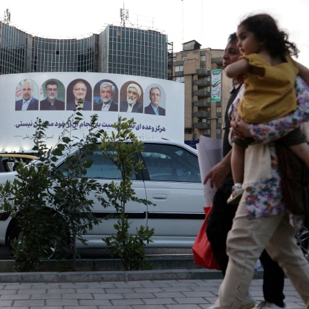 Eine Familie läuft auf einer Straße in Teheran, Ira vor einem Poster, das die Kandidaten der Präsidentschaftswahl zeigt