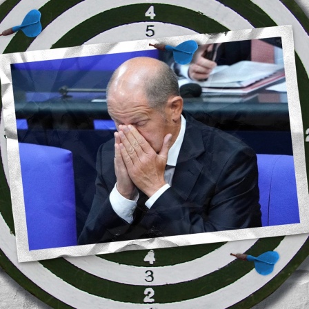 Eine Bildmontage zeigt eine Postkarte auf einer Dartscheibe. Sie zeigt Bundeskanzler Olaf Scholz, der sich die Hände vors Gesicht hält.