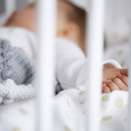 Ein Baby schläft in Rückenlage im Gitterbett