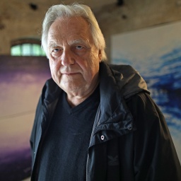 Der Kunstberater Helge Achenbach steht in einem Atelier vor seinen Bildern.