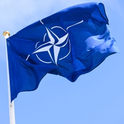 Eine Flagge der Nato weht vor blauem Himmel.
