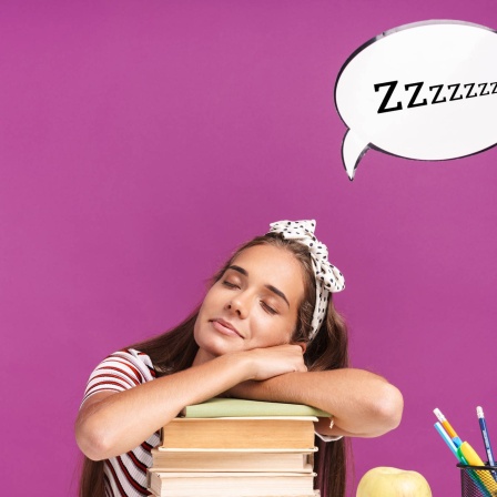 Image of young relaxed girl sitting at desk and sleeping on stack of books. Symbolfoto