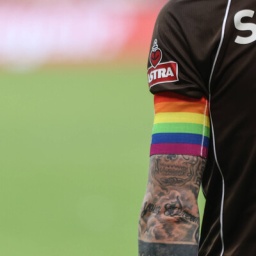 Ein Fußballspieler vom Verein FC Sankt Pauli trägt eine Armbinde in den Farben der Regenbogenflagge.