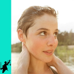 Junge Frau beim Baden am See schaut an der Kamera vorbei nach rechts und streicht sich die Haare aus dem Gesicht