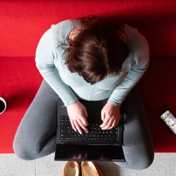 Eine Frau sitzt im Homeoffice auf einer roten Couch und arbeitet an einem Laptop