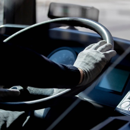 Ein Busfahrer hält das Lenkrad mit Handschuhen.