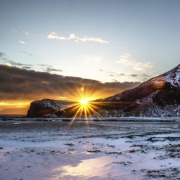 Die Sonne geht hinter schneebedeckten Bergen auf und taucht die winterliche Landschaft in warmes Licht (Island, Europa)