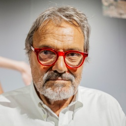 Großaufnahme von Oliviero Toscani, der eine rot gerandete Brille trägt und ernst in die Kamera blickt.