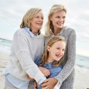 Drei Frauen verschiedener Generationen bzw. Altersklassen stehen gemeinsam lachend am Strand