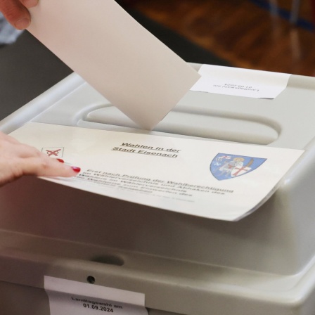 Eine Person wirft einen Wahlzettel in eine Urne in Thüringen.