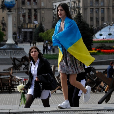 Eine junge Frau trägt die ukrainische Landesfahne über ihren Schultern, als sie auf dem Majdan-Platz, dem Unabhängigkeitsplatz, im Zentrum von Kiew an Panzersperren vorbei geht.