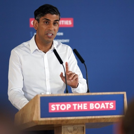 Rishi Sunak spricht während einer Pressekonferenz. An seinem Podium ist der Slogan "Stop the Boats" angebracht.