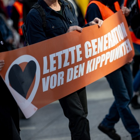 Demonstranten laufen auf einer Demoder Klimagruppe Letzte Generation mit einem Banner mit der Aufschrift “letzte Generation vor den Kipppunkten” über den Potsdamer Platz.