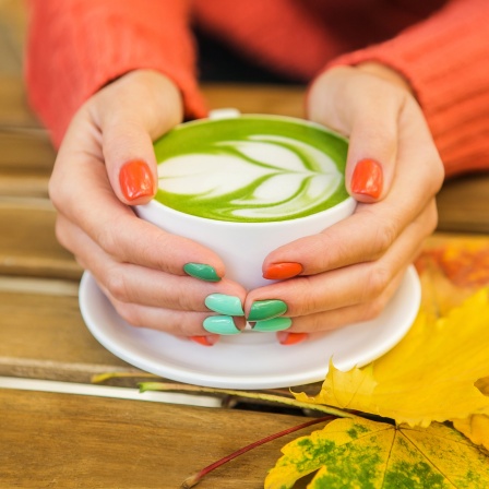 Female hands holding cups of matcha green tea on rustic wooden table background