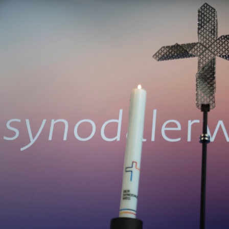 Eine Kerze und ein Kreuz stehen zu Beginn der Dritten Synodalversammlung der deutschen Katholiken vor dem Schriftzug "synodalerweg.de".