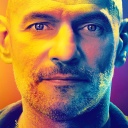 Portrait vom Ex-Polizist Rolf L. Er schaut direkt in die Kamera. Von links ist sein Gesicht orange beschienen, von rechst blau.