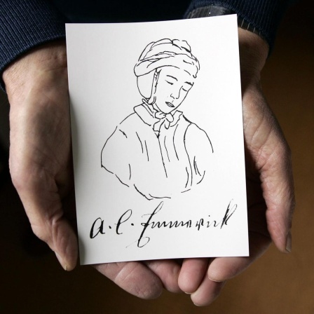 Zwei Hände halten eine Postkarte mit der Zeichnung einer Nonne. Darunter steht in Schreibschrift A.K. Emmerick.