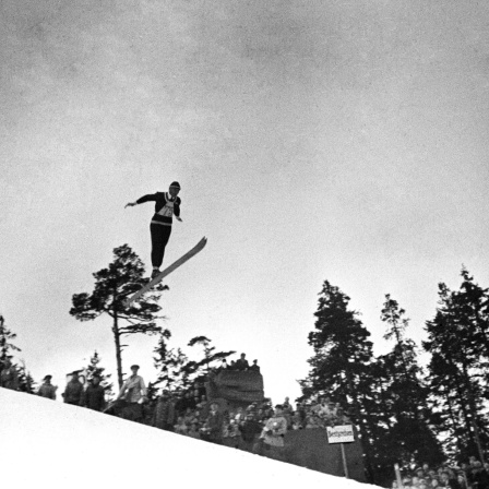 Eine historische Fotografie zeigt den Skispringer Jacob Tullin Thams wie er über einen Abhang fliegt.