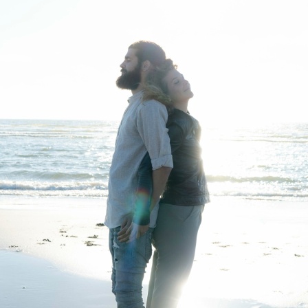 Junges Paar steht Rücken an Rücken am Strand.