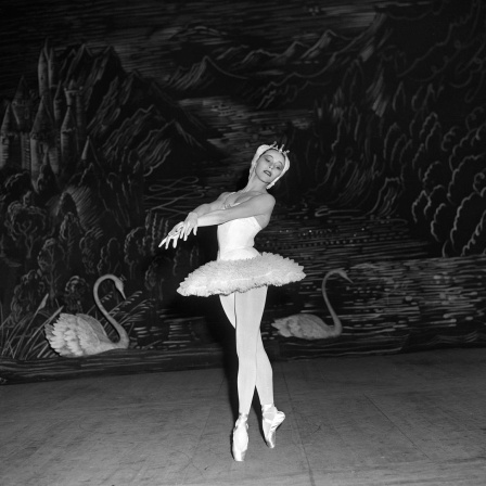 Eine Schwarz-Weiß-Fotografie der Primaballerina Maria Tallchief im New York City Ballet. Sie nimmt eine anmutige Pose ein, während sie Tschaikowsky's Schwanensee tanzt. Sie trägt Tutu und Spitzenschuhe. Im Hintergrund sind Schwäne an der Wand angemalt.