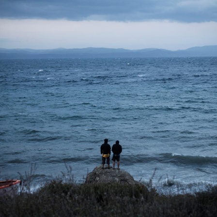 Zwei Personen schauen auf der griechischen Insel Lesbos aufs Mittelmeer in Richtung Türkei.