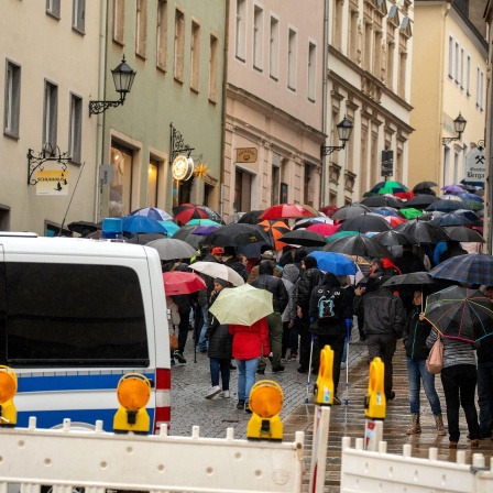 Menschen mit Regenschirmen laufen in Annaberg-Buchholz eine Straße entlang. Im Vordergrund steht ein Polizeifahrzeug