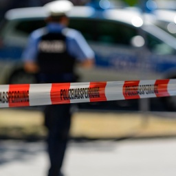 Polizeiabsperrung mit Flatterband, hinten Streifenwagen und Polizeibeamter