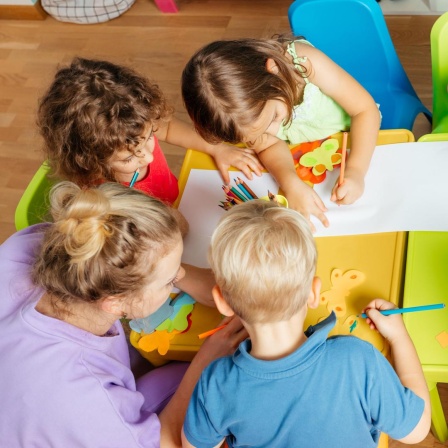 Eine Erzieherin malt mit Kindern in einer KITA.