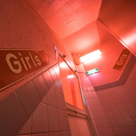 Wegweiser in einem rot ausgeleuchteten Treppenhaus auf denen Girls steht.
