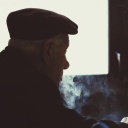 Ein alter Mann von schräg hinten in einem Raum umgeben von Zigarettenrauch