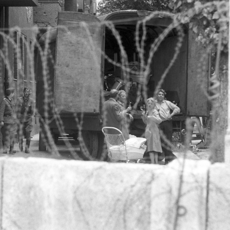 Eine Familie hinter Stacheldraht bewacht von Volkspolizisten der DDR während der Zwangsräumung von Häusern in der Bernauer Straße in Berlin, 1961.