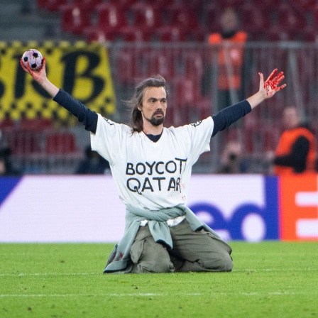Das Beitragsbild Dok5 "Fußballkapitalismus - Ein Fan wird kritisch" zeigt einen Aktivisten auf dem Fußballfeld der ein T-Shirt trägt mit der Aufschrift Boycott Qatar.