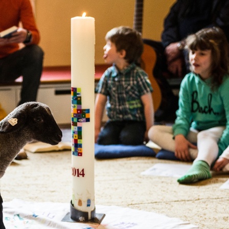 Zwei Lämmchen laufen bei einem Kindergottesdienst an einer Kerze vorbei.