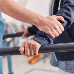 Hände einer Therapeutin stützen Patienten beim Lauftraining in der Physiotherapie 