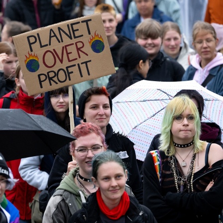 Zahlreiche Menschen nehmen an einer Demonstration zum Klimastreik teil und halten ein Plakat mit der Aufschrift „Planet over profit“ in die Höhe