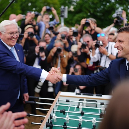 Emmanuel Macron, Präsident von Frankreich, besucht zusammen mit Bundespräsident Frank-Walter Steinmeier das Demokratiefest aus Anlass von 75 Jahren Grundgesetz und sie stehen dabei an einem Tischkicker. 