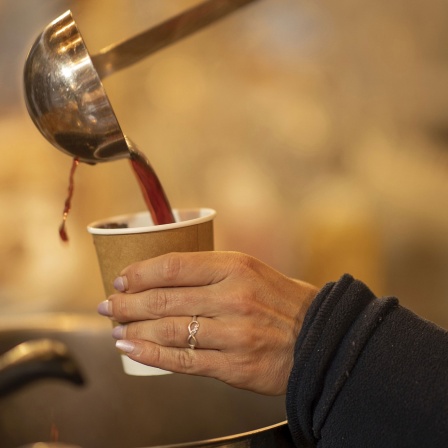 Frau schenkt Glühwein mit einer Kelle in einen Becher ein