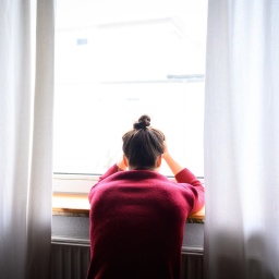 Eine Frau steht am Fenster und wirkt niedergeschlagen