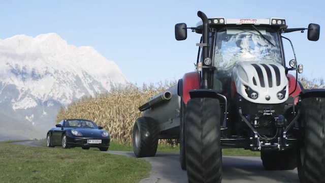 Ein Porsche fährt hinter einem Traktor und kommt nicht vorbei. Szene aus einer Werbung.