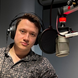 Ein junger Mann sitzt mit Kopfhörern vor einem Mikrophon und blickt in die Kamera. Aufgenommen am 12.03.2025 im NDR Studio Göttingen
