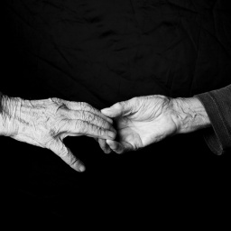 Schwarz-weiß: Zwei Hände mit Falten greifen nach einander.