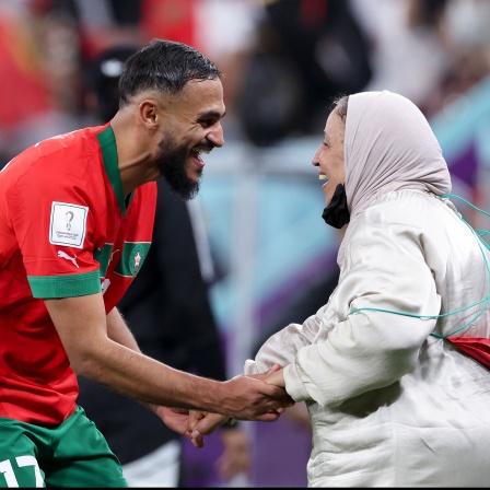 WM in Katar – Marokkos Sofiane Boufal (l) tanzt nach dem Sieg gegen Portugal mit seiner Mutter auf dem Rasen. © picture alliance/dpa/XinHua/Cao Can