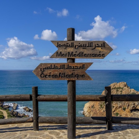 Zwei Schilder mit der Aufschrift Mittelmeer und Atlantik stehen am Kap Aprtel in Marokko, wo Atlantik und Mittelmeer zusammenfließen.