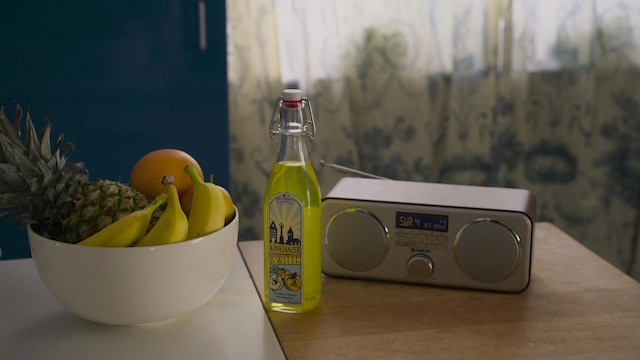 Eine Flasche Likör steht neben einem Radio und einer Schale Obst.