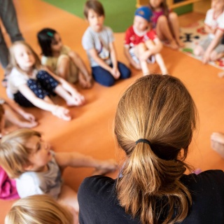 Eine Erzieherin sitzt mit Kindern im Kindergarten im Kreis auf dem Boden