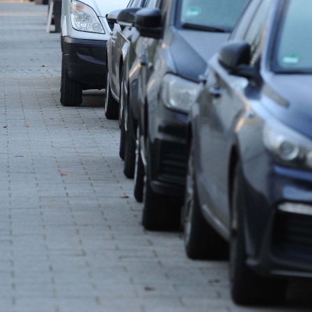 In einer Straße sind Autos zur Hälfte auf dem Gehweg geparkt. 