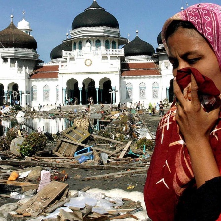 Eine Frau bedeckt ihre Nase mit einem Tuch; im Hintergrund eine Moschee. In den Straßen ist der Müll zu sehen, der sich nach dem Erdbeben und Tsunami in Banda Aceh auf der indonesischen Insel Sumatra im Dezember 2004 angesammelt hat.