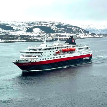 Ein weiß rotes Schiff fährt durch einen Fjord in der Landschaft der Hurtigruten in Norwegen, dahinter eine Landschaft mit Schnee