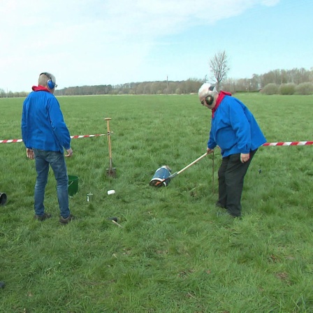 Einwohner von Herzebrock-Clarholz stehen mit Ohrenschützern auf einem freien Feld, einer hält eine brennende Fackel an den Boden einer Milchkanne.